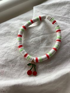 a red and green bracelet with a cherry charm on it's end is laying on a white sheet