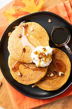 three pancakes on a black plate topped with whipped cream