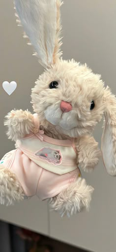 a white stuffed rabbit hanging from the ceiling with hearts in the air behind it and a pink dress on its chest