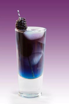 a blue drink with blackberries on the rim in a glass against a purple background