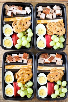 four black trays filled with food on top of a wooden table next to each other