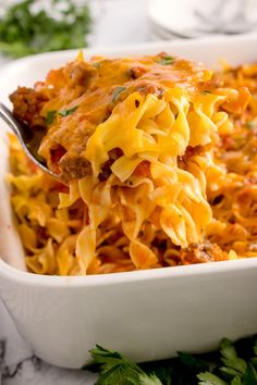 a spoon full of pasta with meat and cheese in a white casserole dish