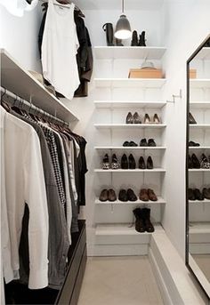 a walk in closet with white shelving and lots of shoes