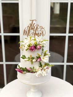 a three tiered white cake with flowers on top and the words, the adventure begins