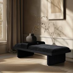 a black bench sitting in front of a window next to a vase on top of a table