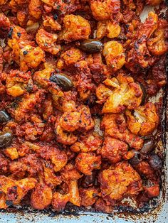 a casserole dish with chicken and olives in tomato sauce, on a blue surface