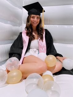 a woman sitting on top of a bed wearing a graduation cap and gown with balloons around her