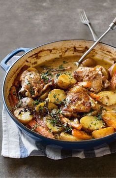 a blue pot filled with meat and potatoes on top of a white towel next to a fork