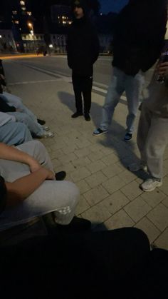 several people sitting on benches at night with one person holding a cell phone and the other standing