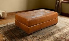 a brown leather ottoman sitting on top of a rug