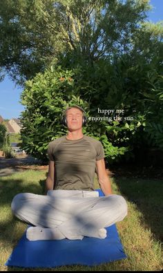 a man sitting on a blue mat in the grass with headphones around his neck