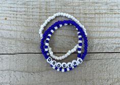 These Dodgers bracelets are the perfect way to show your team pride for the big game! Pair them with any outfit. This listing is for 3 bracelets as shown in pictures.  TO ORDER:  1. Pick bracelet length  2. Pick letter color 3. Submit and I'll get to work :)  PRODUCT DETAILS:  - Bracelets are made with sturdy jewelry elastic - Listing is for three bracelets  - All orders are final. Please double check your bracelet size  CARING TIPS:  - Do not expose jewelry to water  - Treat and store jewelry gently  - Roll bracelets on rather than stretching band to get on  Don't see your teams bracelets on our shop? Or have a custom team bracelet you want? Head to this link to order your custom ones!  https://kanaeohana.etsy.com/listing/1591607617/custom-sports-team-bracelets-team  We are HAPPY to do bu Blue Beaded Bracelets With Letter Beads For Team Spirit, Blue Team Spirit Jewelry For Game Day, Blue Adjustable Beaded Bracelets For Team Spirit, Casual Beaded Bracelets In Team Colors For Sports Events, Casual Team-colored Beaded Bracelets For Sports Events, Casual Blue Jewelry For Game Day, Adjustable Team Spirit Bracelets With Letter Beads, Personalized Team-colored Bracelets For Team Spirit, White Team Spirit Wristbands For Team Events