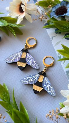 two blue and gold leaf shaped keychains sitting on top of a table next to flowers