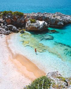 a person is standing in the clear blue water near an island with rocks and sand