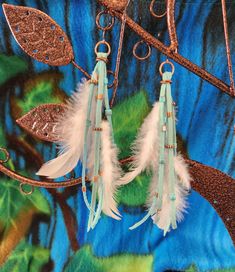 two white feathers hanging from a tree branch with blue and green leaves in the background