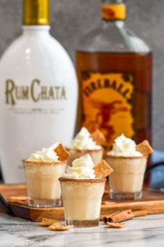 three dessert cups with whipped cream and cinnamon on a cutting board next to a bottle of rumchata