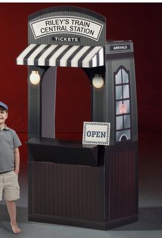 a young boy standing in front of a train station booth with an open sign on it