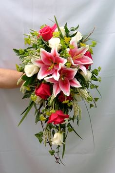 a bridal bouquet with red roses and white lilies is held by someone's hand