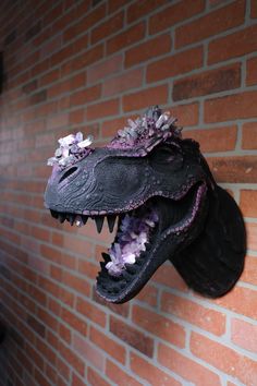 a fake alligator head mounted to the side of a brick wall with flowers on it