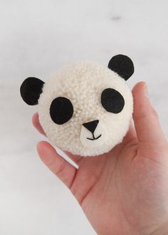 a hand holding a small white and black panda bear brooch on it's palm