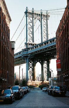 cars are parked in front of some tall buildings and the brooklyn bridge is visible behind them