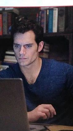 a man sitting in front of a laptop computer on top of a desk next to a book shelf