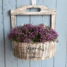 a wooden bucket filled with purple flowers hanging from the side of a blue wall next to a door