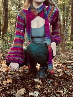 a woman is sitting in the woods wearing a colorful knitted sweater and green leggings