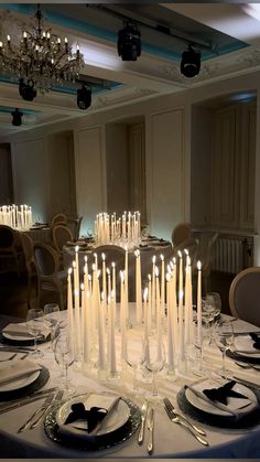 a table with many white candles on it and plates in front of the centerpiece