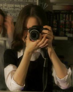 a woman taking a selfie in front of a mirror with a camera on her shoulder