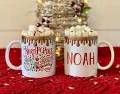 two mugs with hot chocolate and marshmallows on them sitting next to a christmas tree