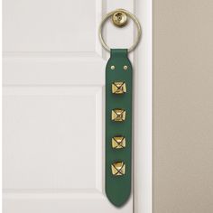 a green leather key holder hanging on the front door with gold studded metal handles