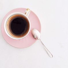 a pink plate topped with a cup of coffee and a spoon