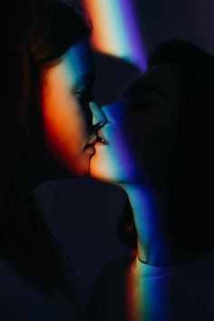 two women are kissing in the dark with colored light coming from their faces behind them