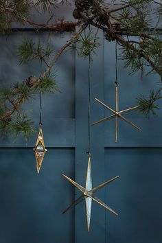 three ornaments hanging from a tree branch in front of a blue wall with pine needles