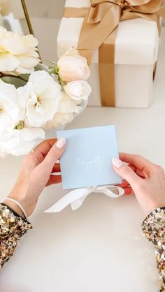 two hands holding a card with the word happy birthday on it, next to a bouquet of flowers