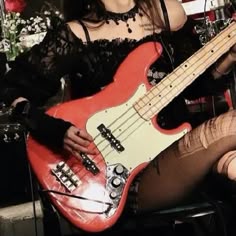 a woman sitting in a chair with a red bass guitar on her lap and wearing black stockings