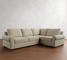 a beige sectional couch sitting on top of a wooden floor next to a white wall