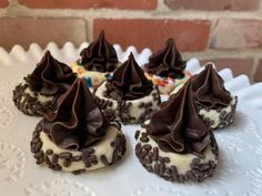 four cookies with chocolate frosting and sprinkles on a white cake plate