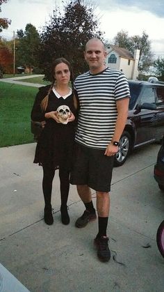 a man and woman standing next to each other in front of a car on the sidewalk