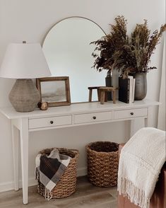 a white console table with two baskets and a mirror on it, next to a lamp