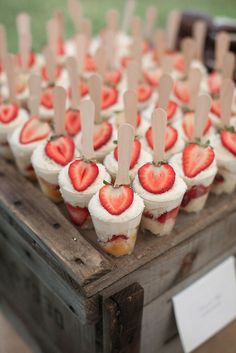 cupcakes with strawberries are arranged on a wooden box and placed on skewers