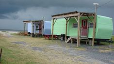 three tiny houses on stilts in front of the ocean under a cloudy sky with storm clouds