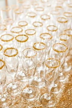 champagne glasses are lined up on a table with gold glitter and sparkles in the background