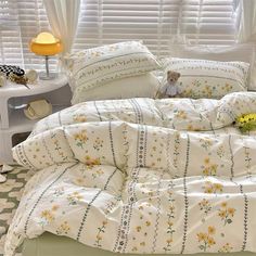 a white bed with yellow flowers on the comforter and pillows in front of a window