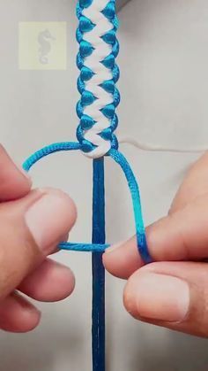 two hands are working on an object with blue and white yarn