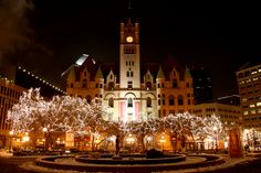 a clock tower is lit up at night in front of a building with christmas lights