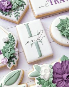 decorated cookies with purple and white flowers are on a table next to the words i, t, and f