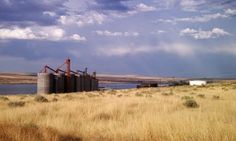 an old grain silo sitting in the middle of a dry grass field next to a body of water