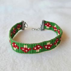 a green and red beaded bracelet with silver clasps on a white cloth background